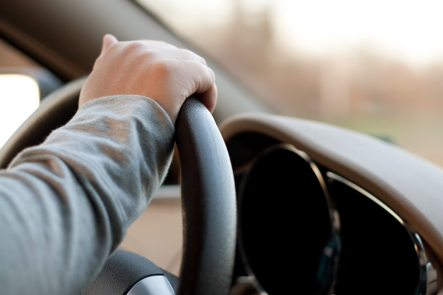 A woman holding the steering wheel of a car with one hand while driving.