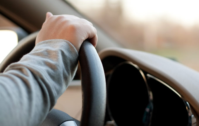 A woman holding the steering wheel of a car with one hand while driving.